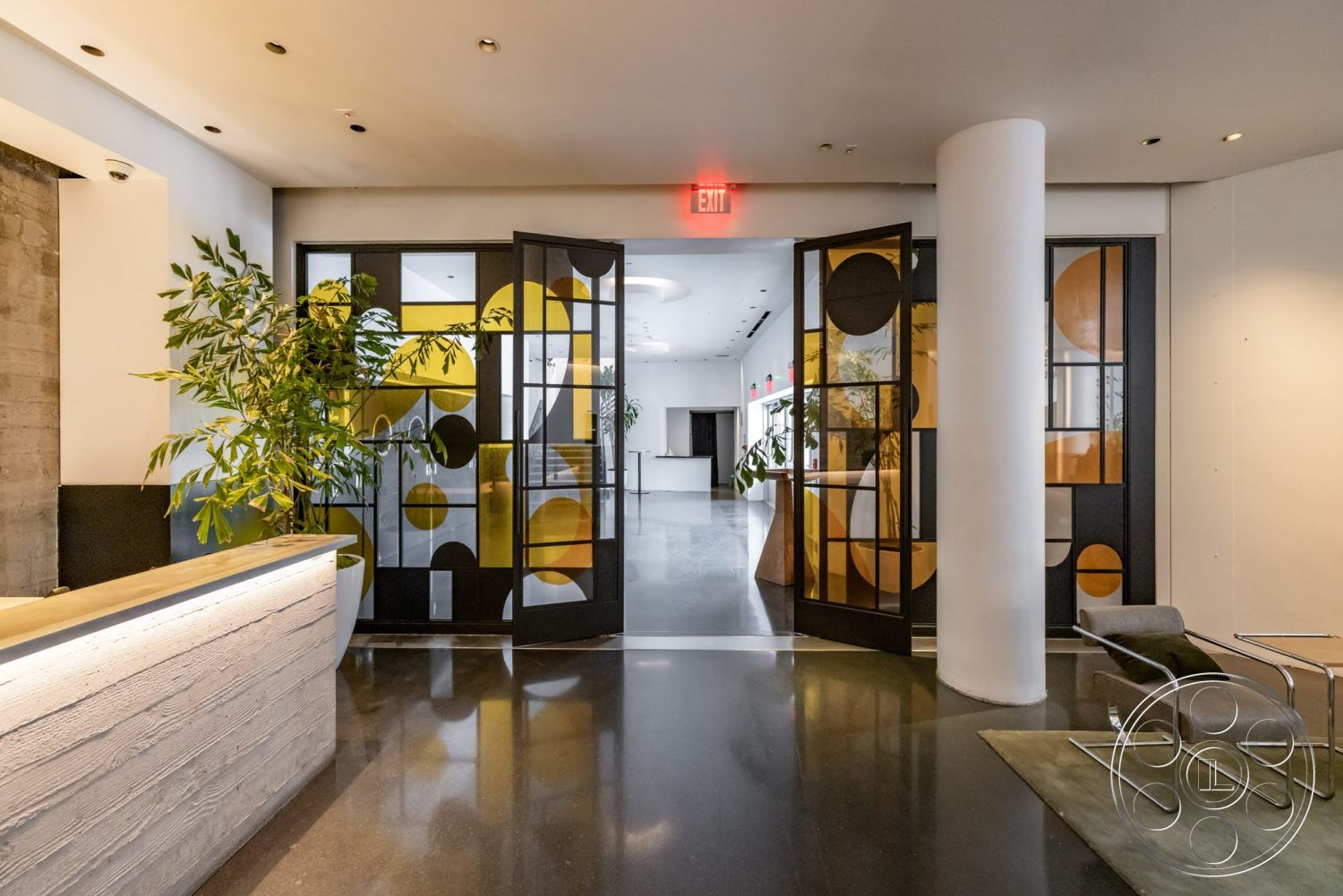 Sunset Campus - polished concrete flooring, open space layout, soft area rug, ambient lighting fixtures, potted indoor plants, floor-to-ceiling glass doors, textured concrete reception desk, highlighted wood countertop, decorative black metal door frames, geometric glass window panes, minimalist lounge chair
