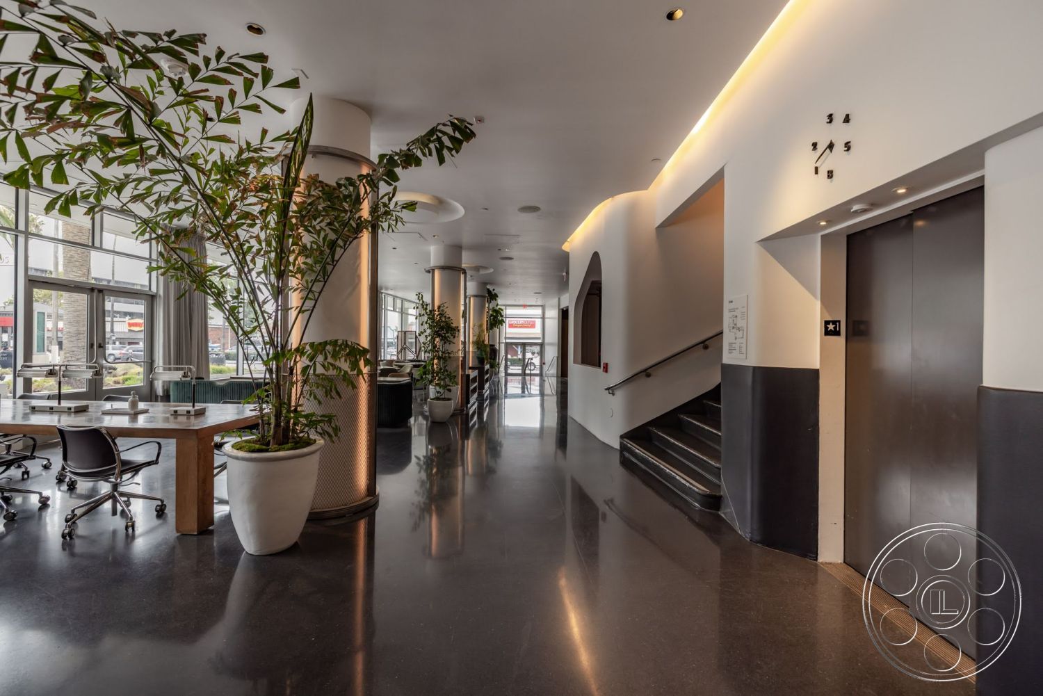 Sunset Campus - neutral color palette, minimalist design, open floor plan, polished concrete flooring, track lighting, glass windows, metal stair railings, modern elevator doors, wood conference table, exposed columns, artificial plants, rounded wall openings