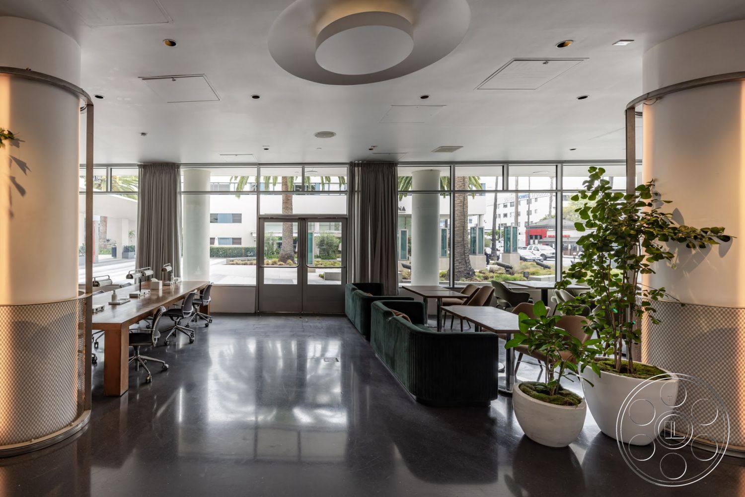 Sunset Campus - polished concrete flooring, floor-to-ceiling windows, textured wall paneling, decorative potted plants, green velvet sofa, modern lounge area, round ceiling light fixture, metal office chairs, wood conference table, industrial-style columns, plaster ceiling, sheer curtain wall treatments