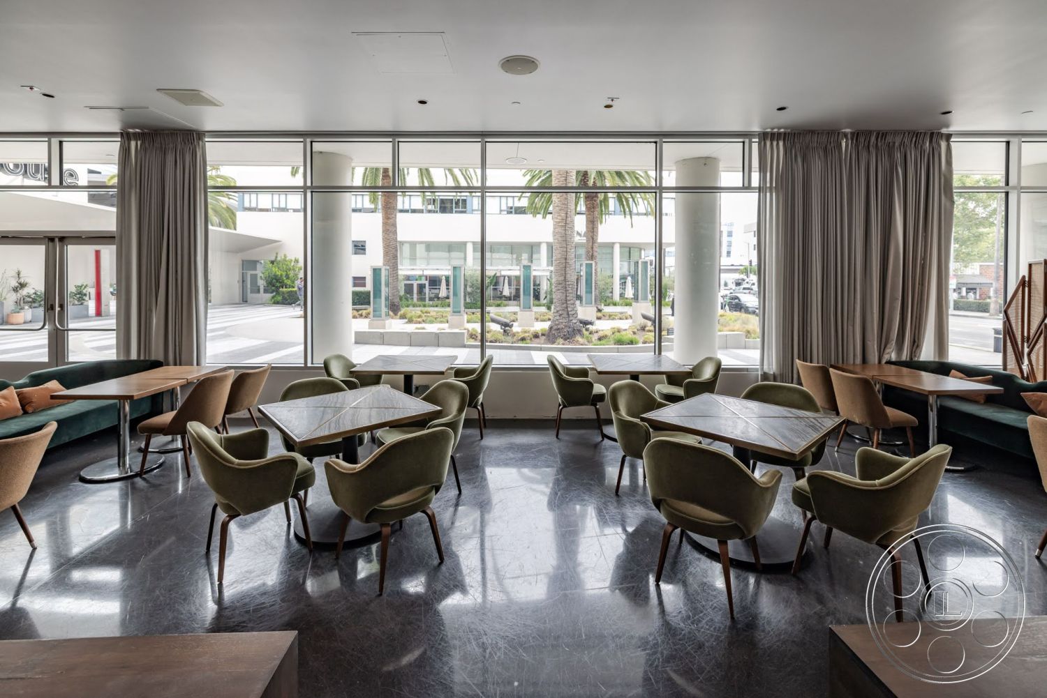 Sunset Campus - neutral color palette, natural light, casual dining area, polished stone flooring, floor-to-ceiling glass windows, concrete column supports, mid-century modern chairs, rectangular wooden tables, tall indoor plants, modern curved seating, heavy fabric drapery