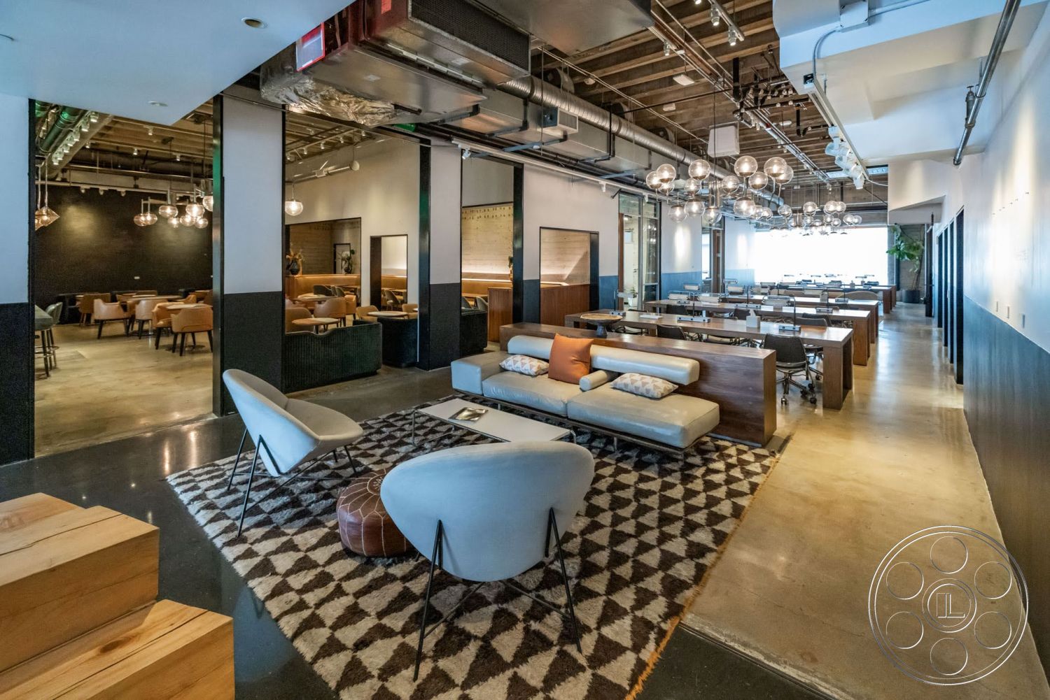 Sunset Campus - minimalist decor, polished concrete floor, wooden ceiling beams, exposed ductwork, geometric area rug, casual meeting area, black accent wall, modern lounge seating, open floor layout, industrial pendant lighting, half-height wooden partition, chair and table workspace, glass conference room doors, half-painted wall (dark blue and white)