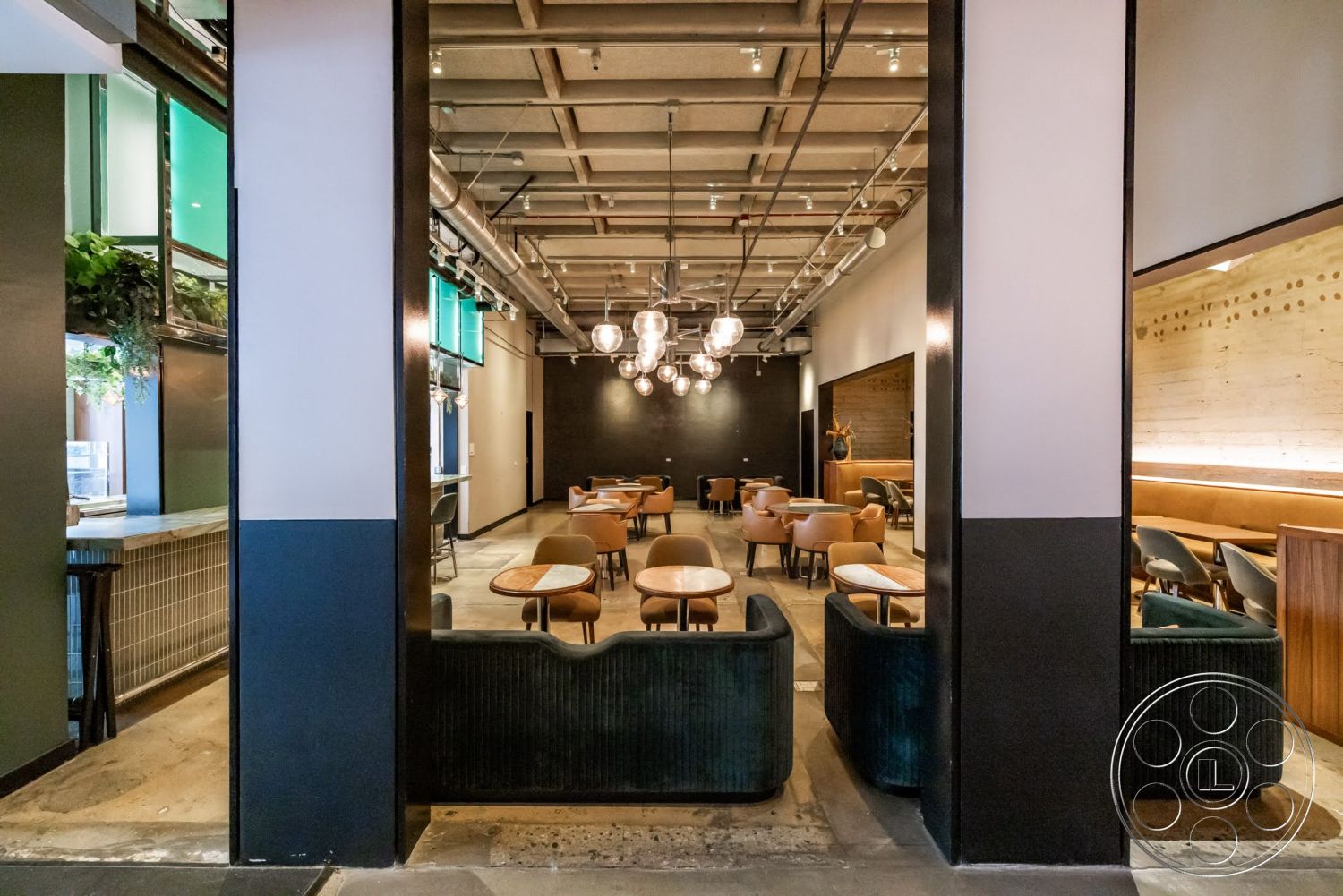 Sunset Campus - polished concrete floor, exposed concrete ceiling, upholstered seating, black accent wall, industrial light fixtures, glass partition windows, wooden table surfaces, green wall plants, wood panel accents, open dining layout, modern restaurant design