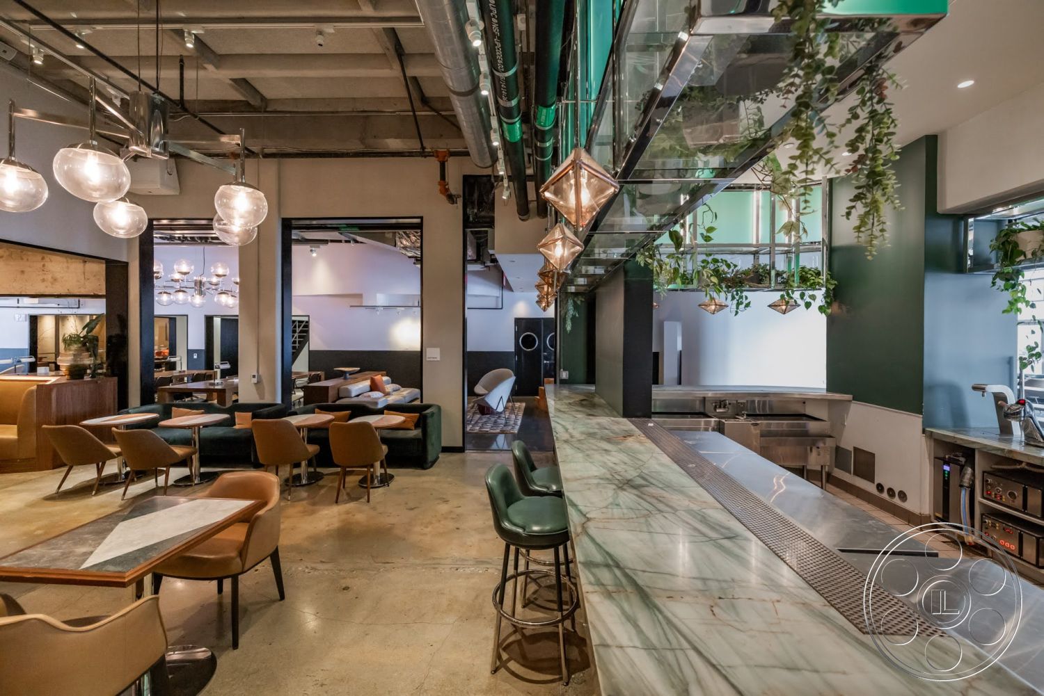 Sunset Campus - polished concrete floor, wood paneling, upholstered dining chairs, industrial decor elements, green accent wall, exposed concrete ceiling, modern bar area, open layout design, pendant light fixtures, marble bar countertop, stylish lounge seating, glass shelving with plants