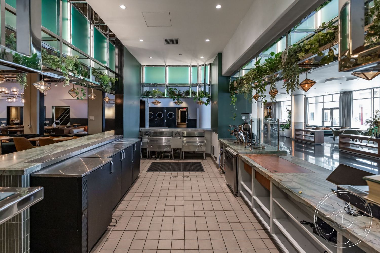Sunset Campus - hanging plants, open dining area, metal light fixtures, exposed ceiling structure, modern industrial design, built-in kitchen appliances, stainless steel countertop, tile kitchen floor, green glass wall panels, concrete bar surface