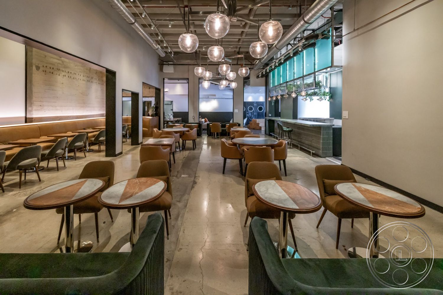 Sunset Campus - neutral color palette, polished concrete flooring, soft ambient lighting, casual dining atmosphere, industrial style decor, glass window wall, marble table tops, modern leather seating, wood accent wall with text, metal ceiling with exposed piping, round pendant lighting fixtures, steel table bases, tufted velvet upholstery, open dining area layout, green tile bar counter