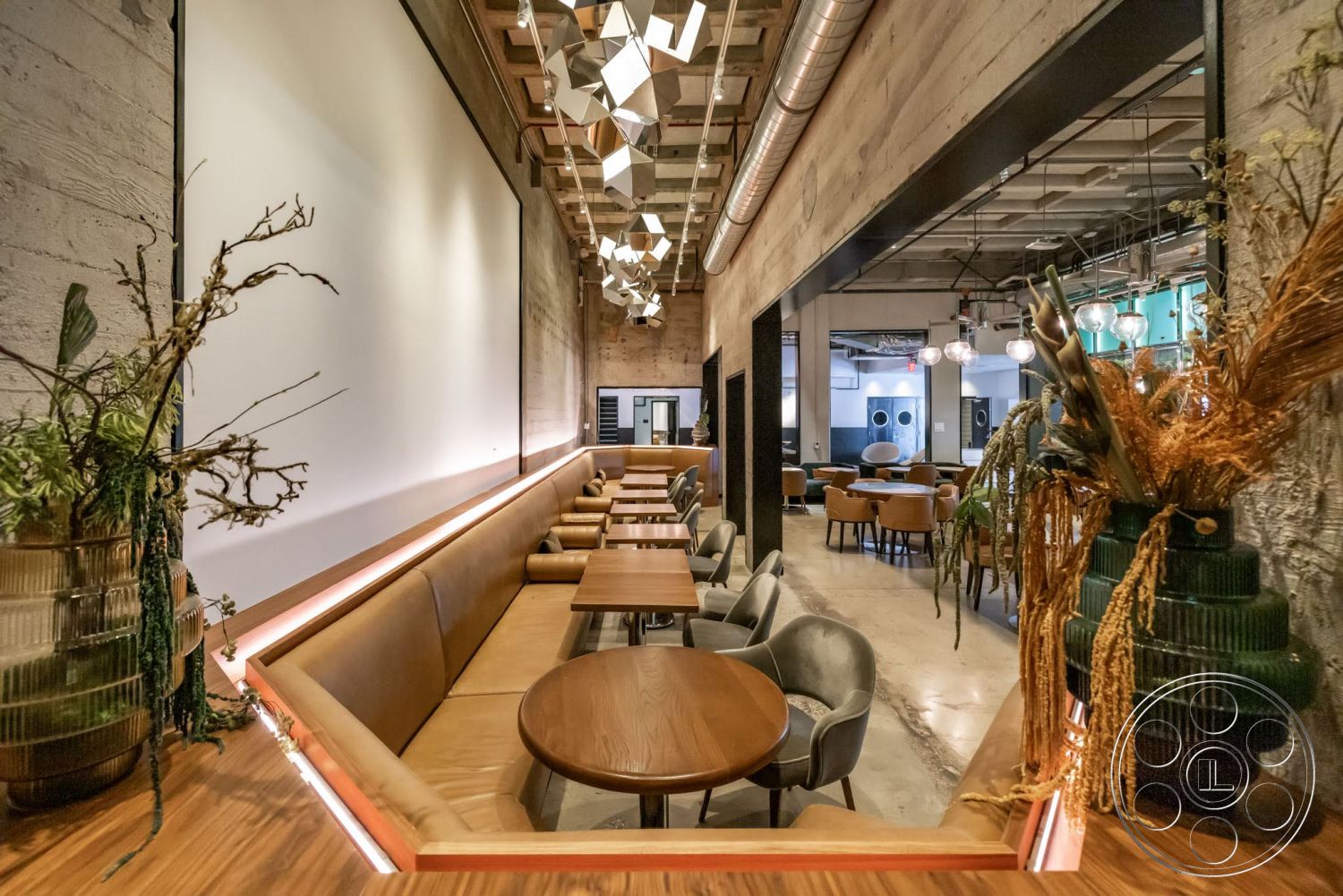 Sunset Campus - polished concrete floor, exposed concrete walls, industrial lighting fixtures, soft ambient lighting, plant decorations, wood beam ceiling, wood dining tables, modern restaurant design, leather bench seating, open-layout interior
