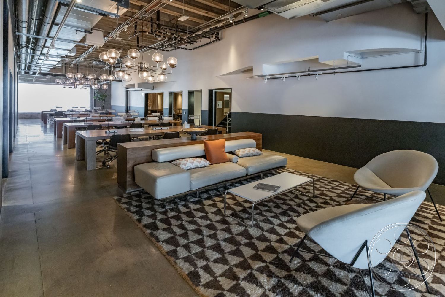 Sunset Campus - textured area rug, modern light fixtures, concrete flooring, industrial design elements, dark accent wall, minimalist coffee table, glass partition walls, white painted walls, exposed ductwork ceiling, metal office chairs, open workspace layout, wood conference tables, sofa with decorative cushions