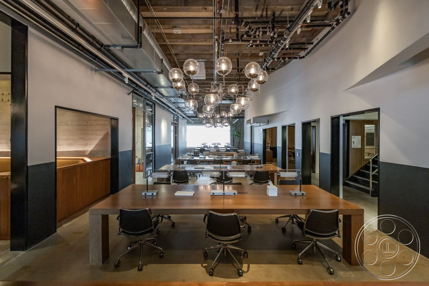 Sunset Campus - dark wood cabinetry, concrete flooring, collaborative workspace, floor-to-ceiling windows, conference area, exposed ductwork, black accent walls, open office layout, wood beam ceiling, white painted walls, rectangular conference tables, glass office partitions, modern office chairs, hanging globe pendant lights