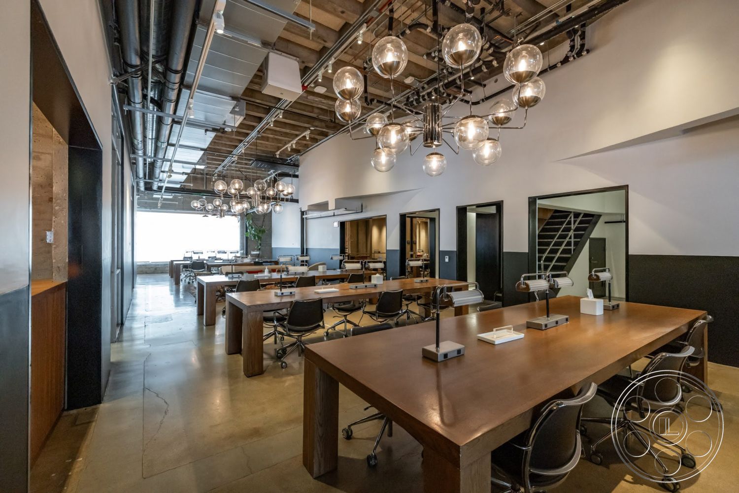 Sunset Campus - concrete flooring, floor-to-ceiling windows, glass light fixtures, black accent walls, open office layout, natural light ambiance, exposed ductwork ceiling, interior workspace, modern industrial style, metal chair legs, wooden conference tables
