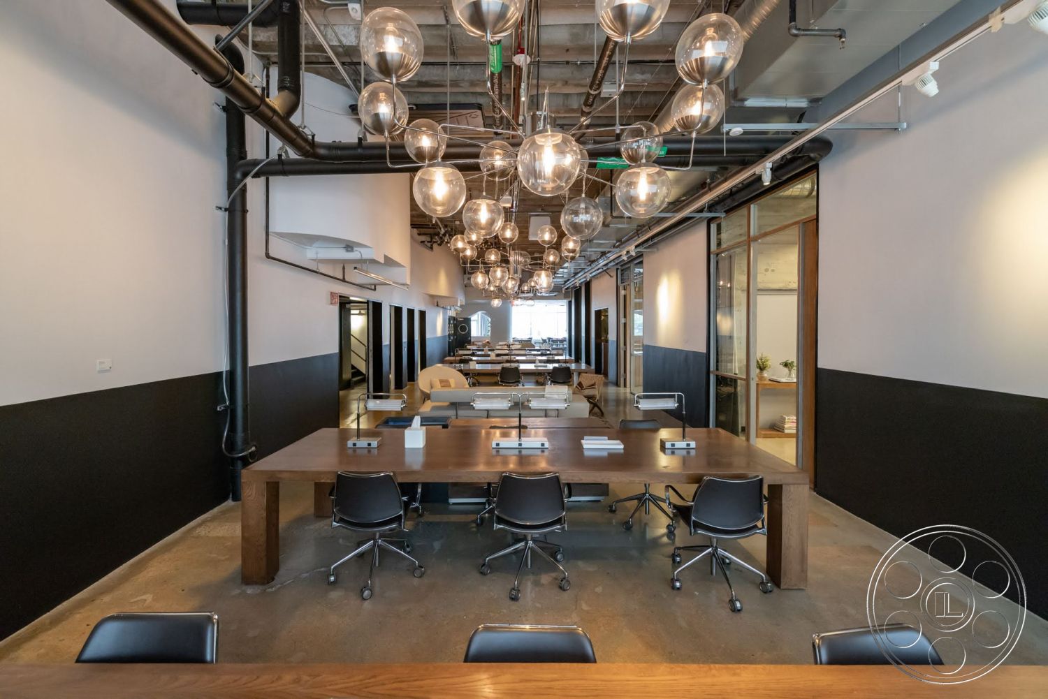 Sunset Campus - concrete flooring, large glass windows, exposed ductwork, black accent walls, metal light fixtures, pendant lighting fixtures, open office layout, white painted walls, black leather office chairs, modern industrial style, ceiling-mounted light fixtures, long wooden conference table
