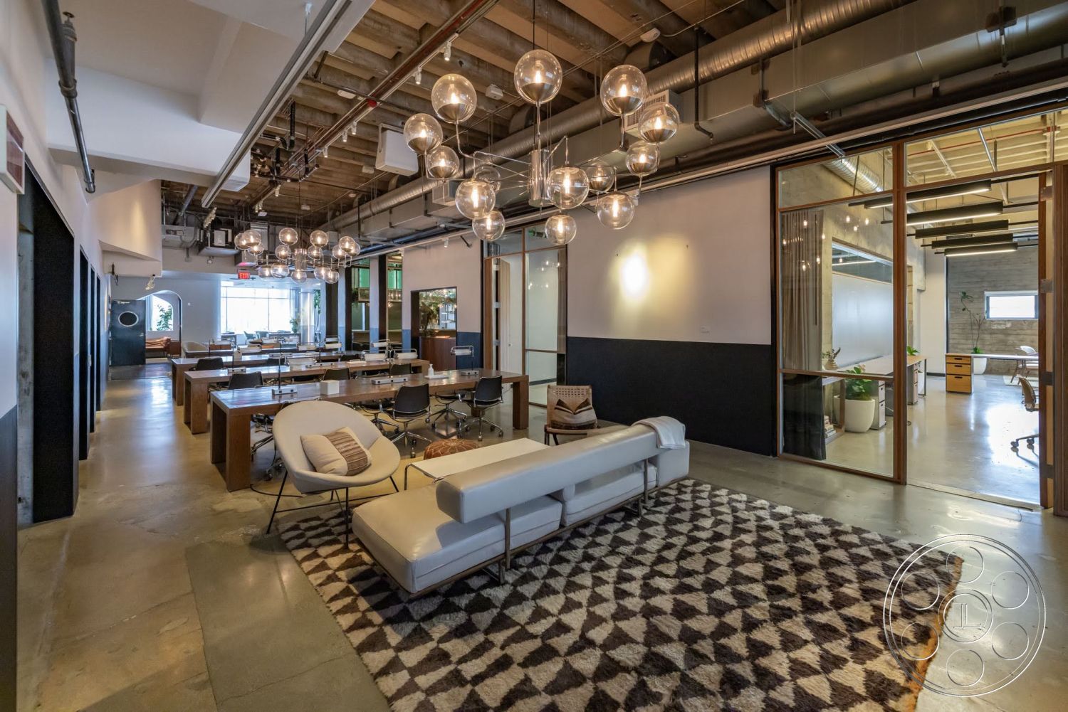 Sunset Campus - minimalist decor, concrete flooring, modern pendant lighting, industrial style, functional workspace, geometric area rug, exposed ceiling beams, open office layout, glass partition walls, wooden conference tables, upholstered modern sofa