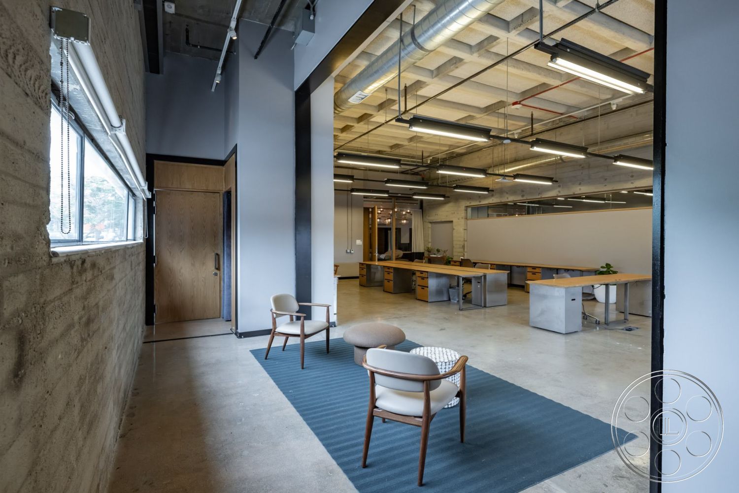 Sunset Campus - concrete flooring, exposed concrete walls, textured ceiling, open office layout, recessed lighting fixtures, modern office furniture, cubicle partitions, wood paneling door, ceiling-mounted air ducts