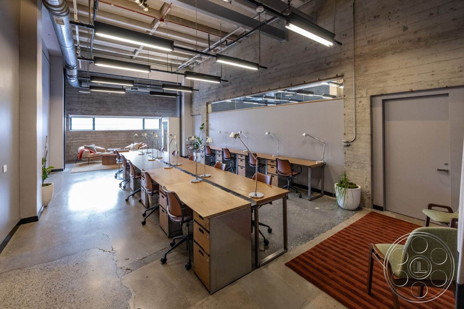 Sunset Campus - concrete flooring, minimalist design elements, exposed concrete walls, floor-to-ceiling windows, woven area rug, textured wall treatment, decorative potted plants, open-plan layout, modern desk setup, interior office space, wooden conference table, industrial style ceiling, task lighting fixtures, metal desk chairs, sectioned workspaces
