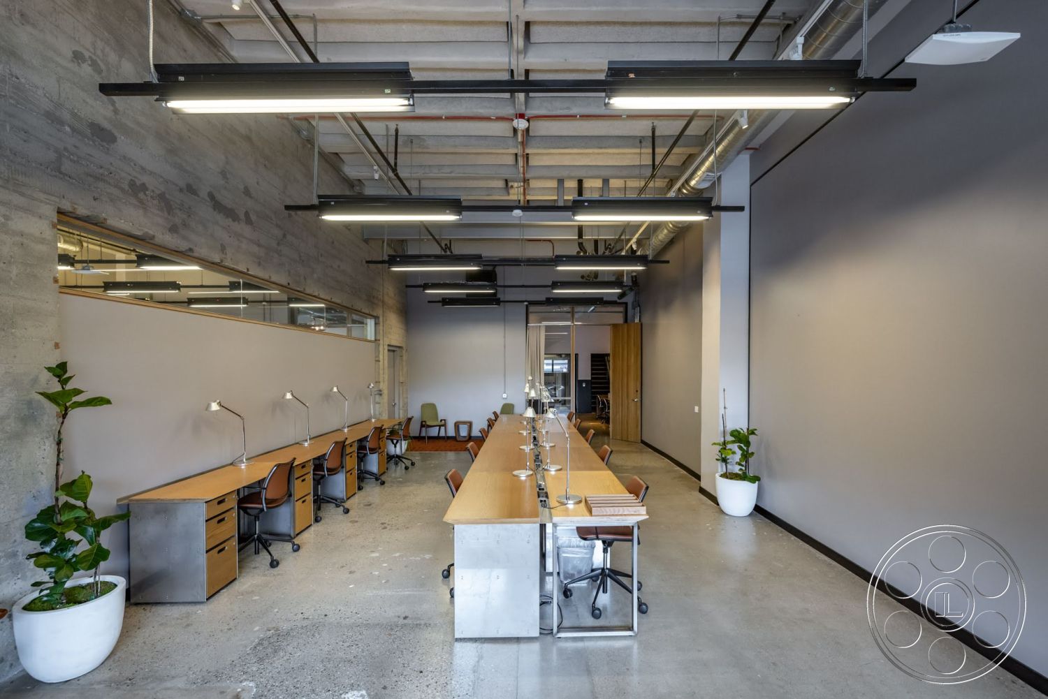 Sunset Campus - high ceilings, neutral color palette, plant accents, concrete flooring, exposed concrete walls, industrial lighting fixtures, open office layout, glass partition walls, modern office design, wooden work desks, metal desk bases