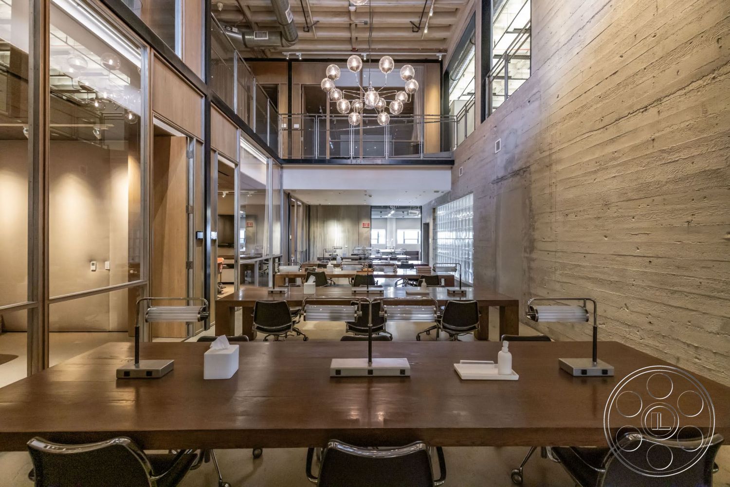 Sunset Campus - high ceilings, polished concrete flooring, exposed concrete walls, industrial style, collaborative workspace, contemporary lighting fixtures, glass partition walls, modern office layout, metal chair frames, hardwood tabletops, open ceiling with ductwork, glass window systems, rustic wood accent walls