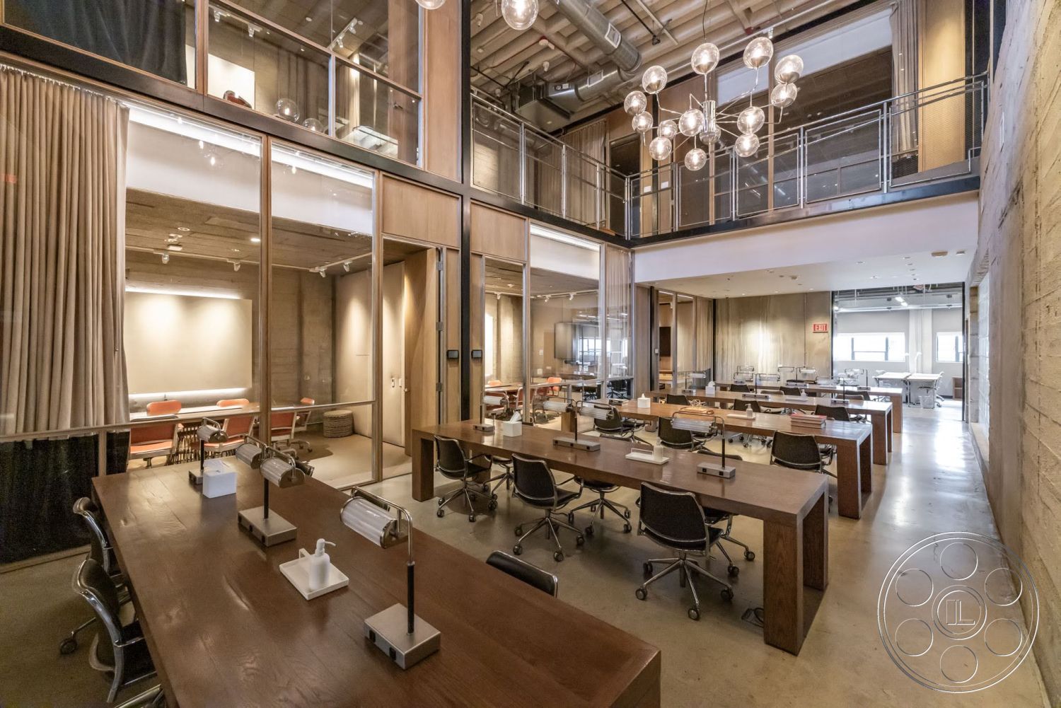 Sunset Campus - concrete floors, natural light from large windows, open office layout, glass partition walls, modern chandelier lighting, wood panel accent wall, exposed ductwork ceiling, metal office chairs, wooden conference tables, soft curtain dividers