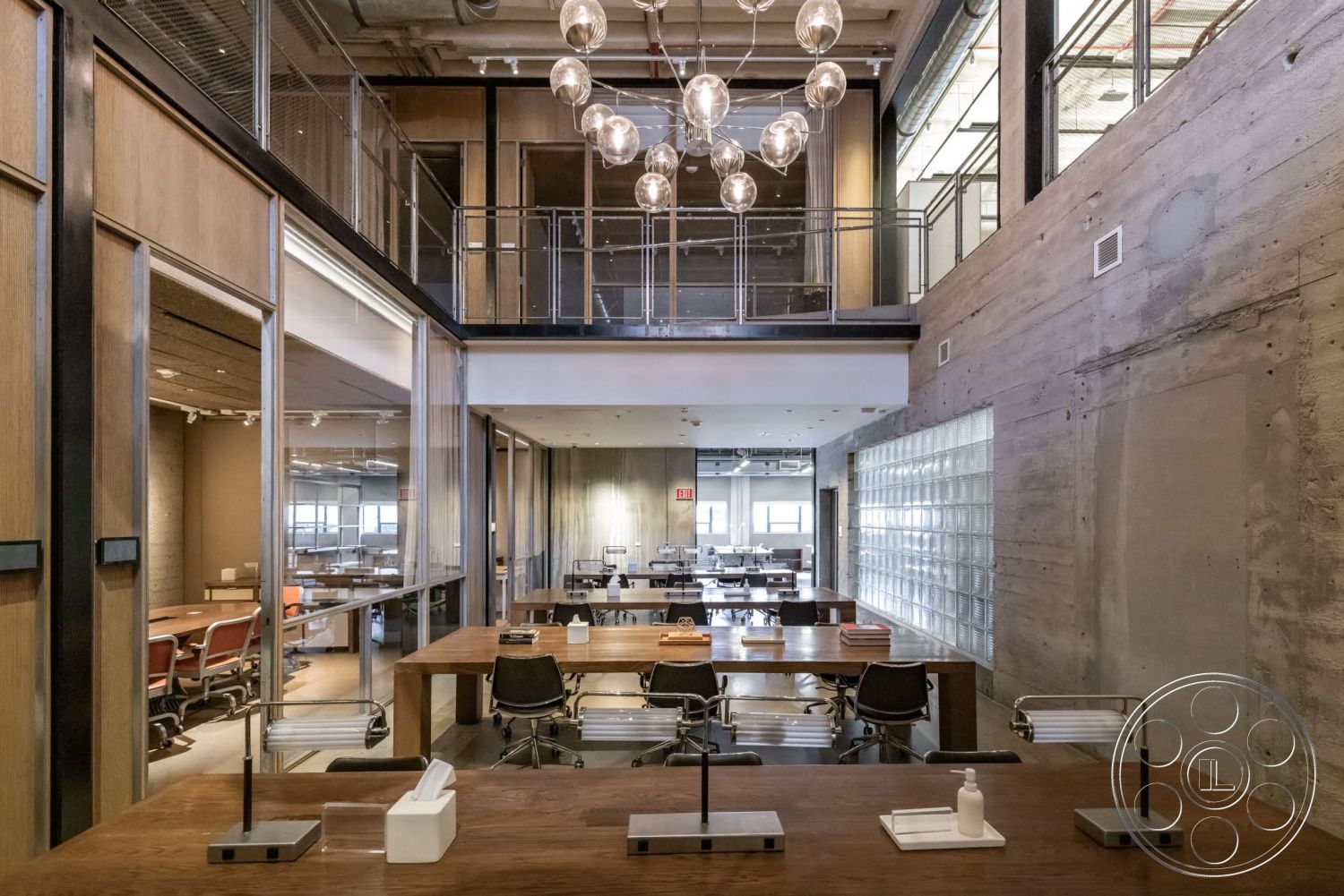 Sunset Campus - open floor plan, modern pendant lighting, exposed concrete walls, concrete ceiling, industrial style chandelier, steel railings, wood paneling accents, metal office chairs, floor-to-ceiling glass partitions, glass block windows, shared workspace area, rectangular meeting tables
