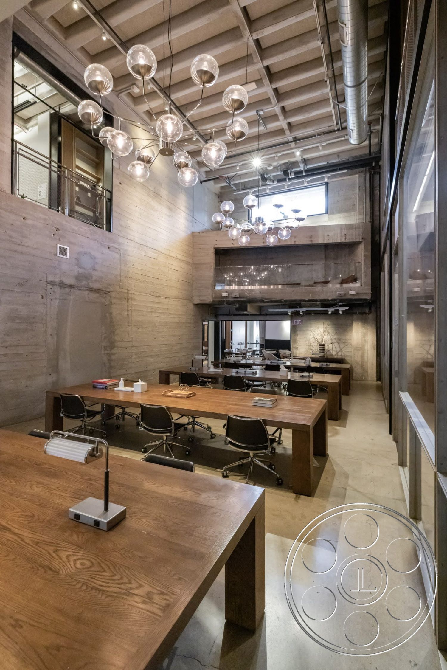 Sunset Campus - concrete flooring, exposed concrete walls, open office layout, industrial-style architecture, large windows with natural light, metal office chairs, high ceilings with exposed beams, wooden conference tables, suspended glass lighting fixtures