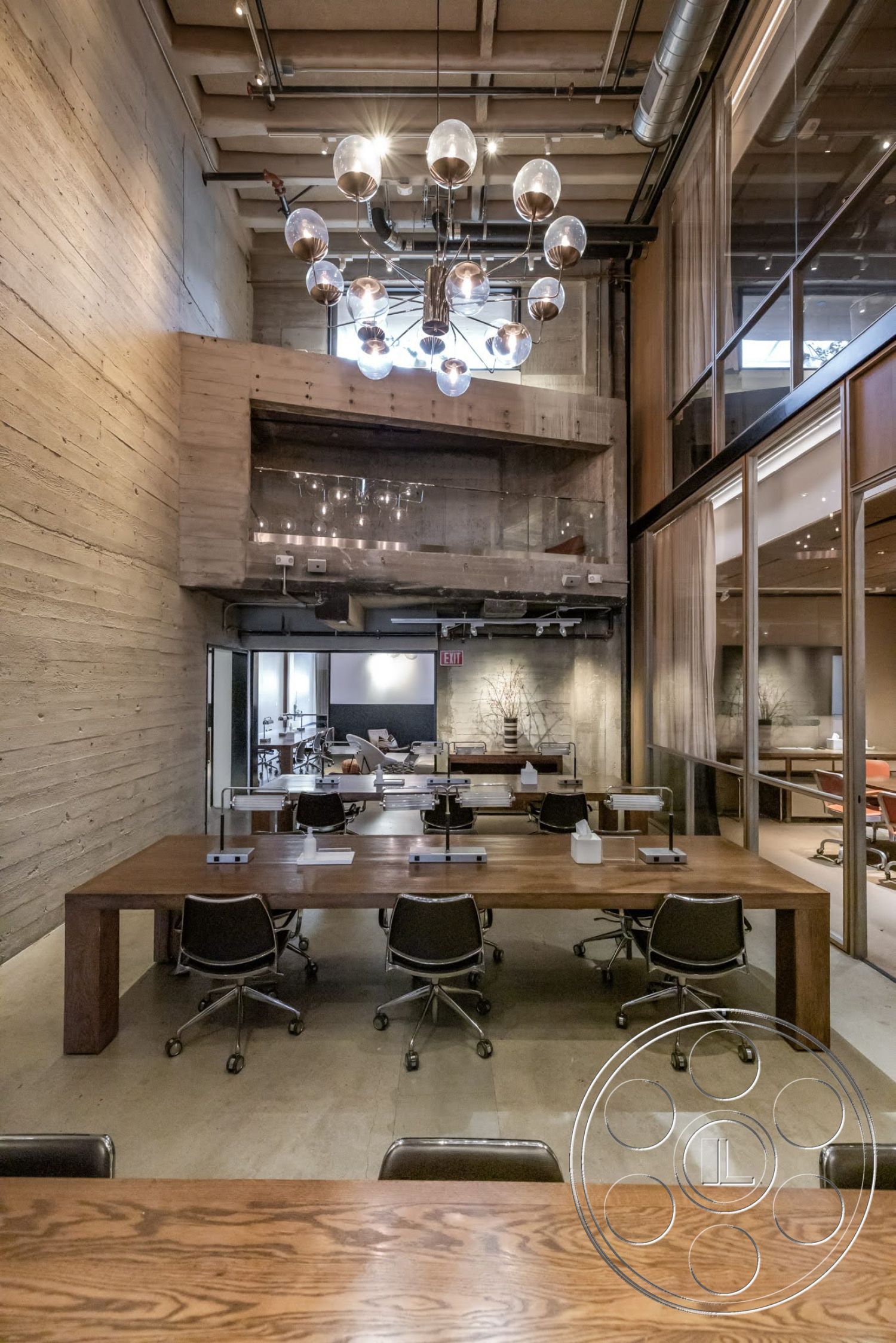 Sunset Campus - neutral color palette, polished concrete flooring, creative workspace, exposed concrete walls, glass partition walls, modern chandelier lighting, wooden conference table, metal swivel office chairs, industrial style open space, vaulted ceiling with beams