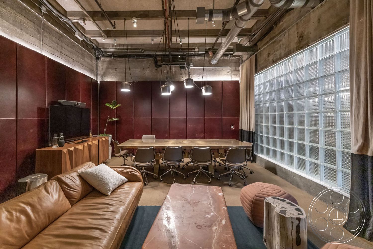 Sunset Campus - concrete walls, industrial lighting fixtures, carpeted flooring, wooden side table, exposed concrete ceiling, brown leather sofa, textured fabric curtains, metal office chairs, wooden conference table, glass block windows, red leather accent wall