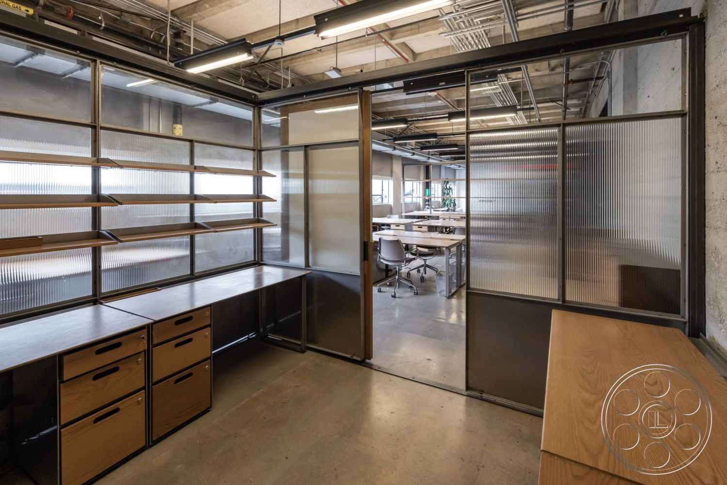 Sunset Campus - polished concrete flooring, exposed concrete walls, industrial lighting fixtures, open office layout, modern office space, multi-functional workspace, built-in wooden shelving units, metal framed glass partition walls, refined wood desktop surfaces