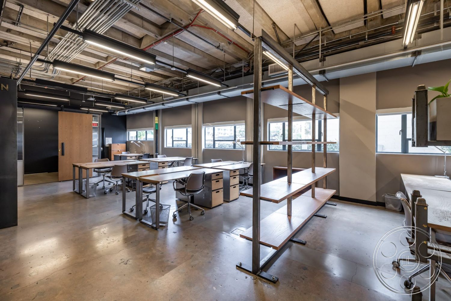 Sunset Campus - exposed concrete floor, glass windows providing natural light, black painted accent wall, open ceiling design with exposed ductwork, metal shelving unit with wooden shelves, industrial-style office space, modular desks with metal frames and wooden surfaces, contemporary office chairs with ergonomic design, modern light fixture design, interior office layout