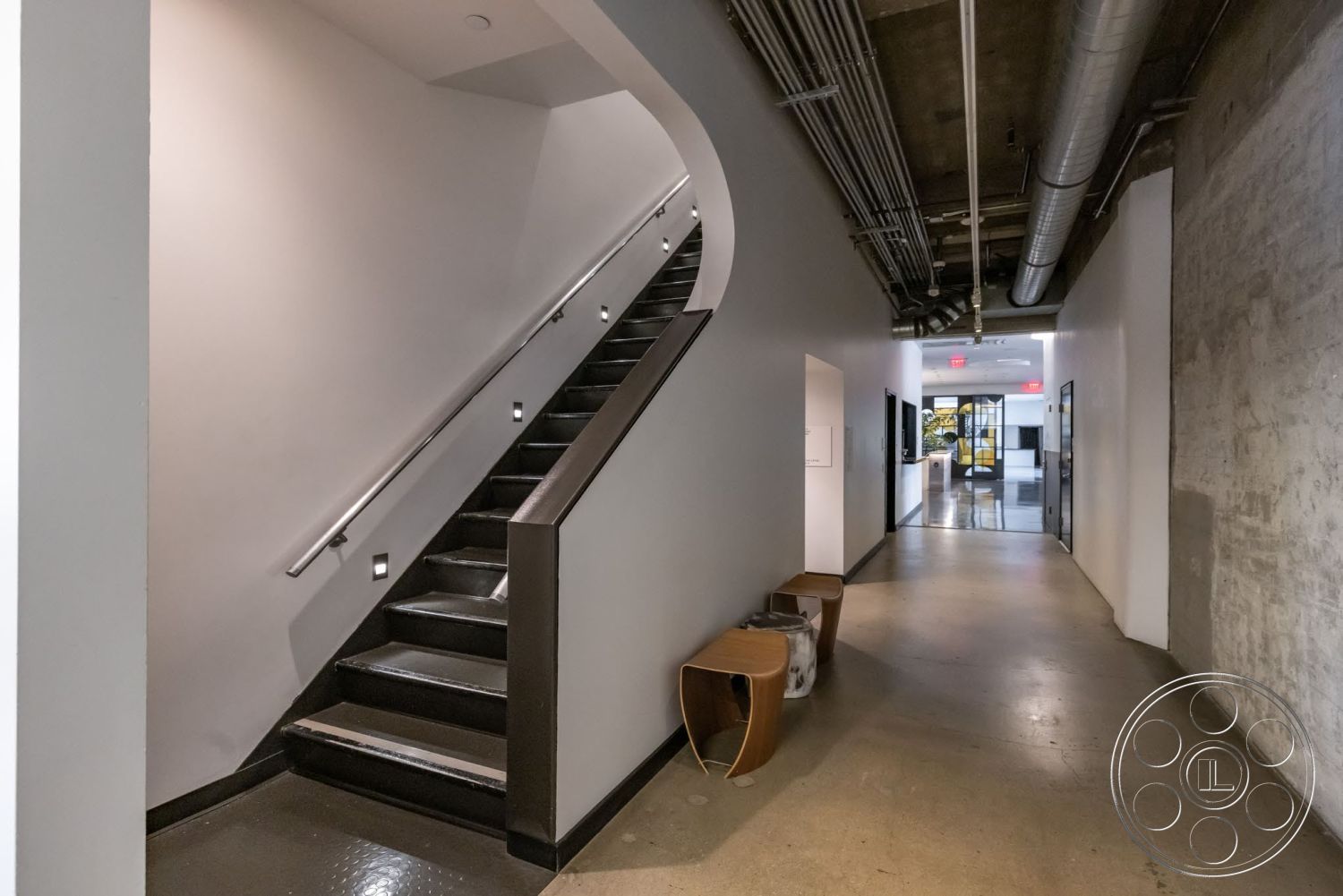 Sunset Campus - open floor plan, white painted walls, exposed ductwork ceiling, modern design aesthetic, concrete floor hallway, metal staircase with black finish, LED wall sconces