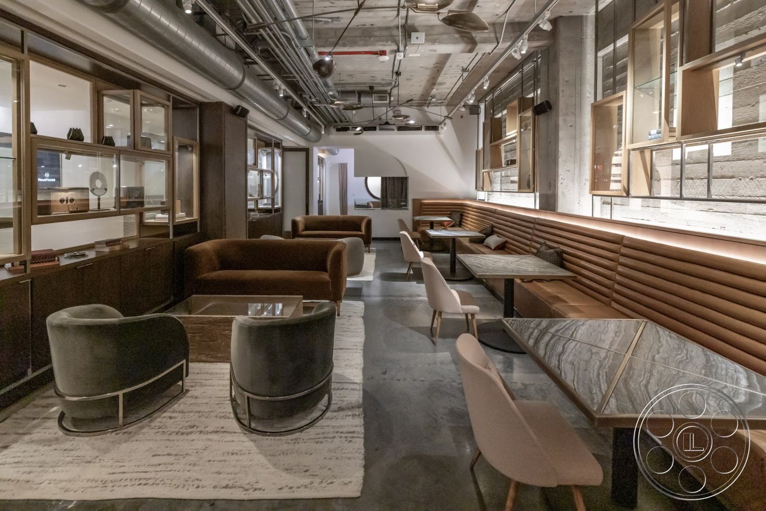 Sunset Campus - minimalist decor, concrete flooring, exposed concrete walls, glass display cabinets, dark wood shelves, velvet upholstered chairs, modern industrial design, curved seating arrangement, wood paneling wall, linear recessed lighting, metal ductwork ceiling, marble table tops, brown leather seating, black metal chair legs