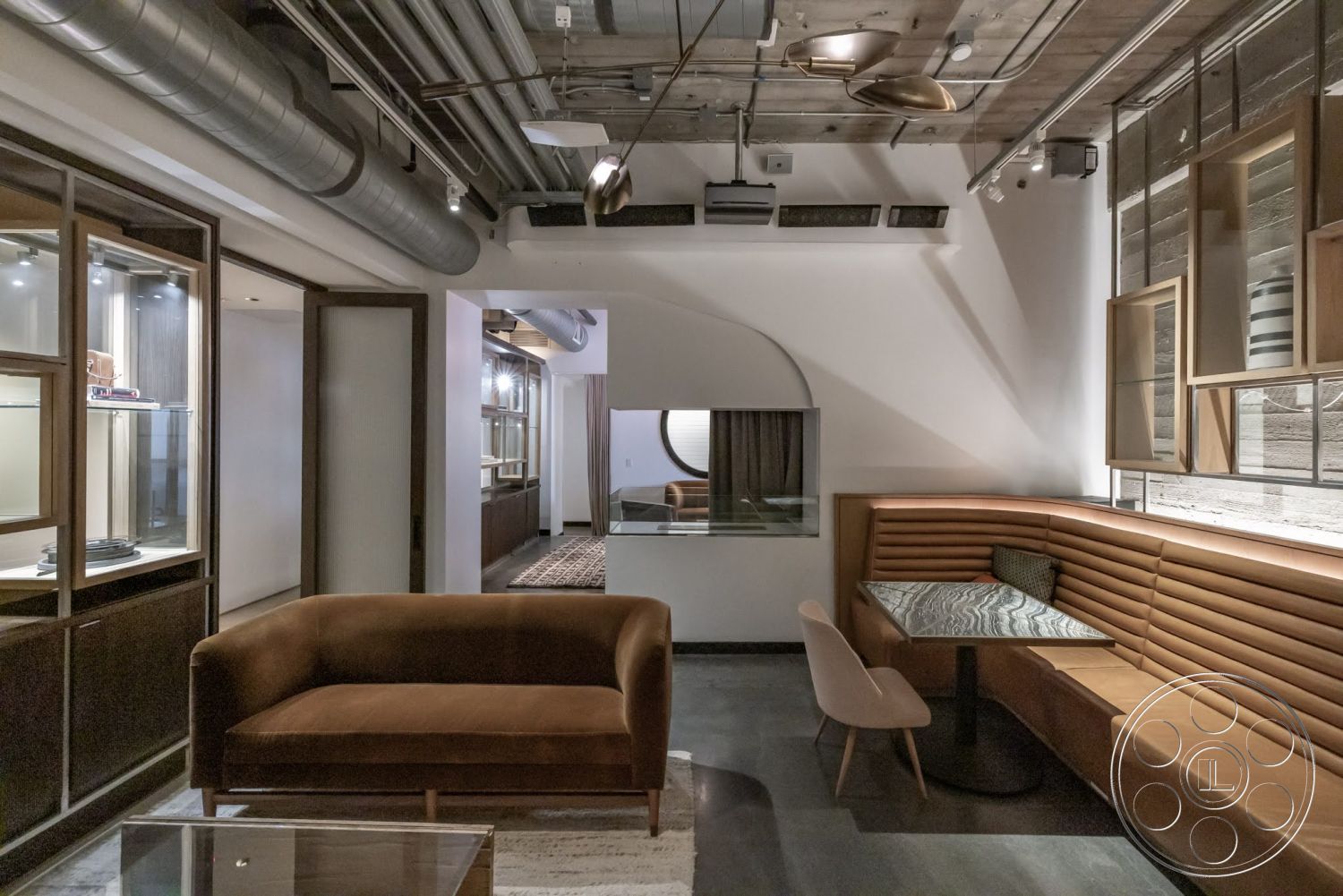 Sunset Campus - dark wood cabinetry, wood accent wall, exposed concrete ceiling, glass display cabinets, black polished concrete floors, modern recessed lighting, smooth plaster walls, metal ductwork ceiling, marble table surface, brown velvet sofa, striped fabric booth seating