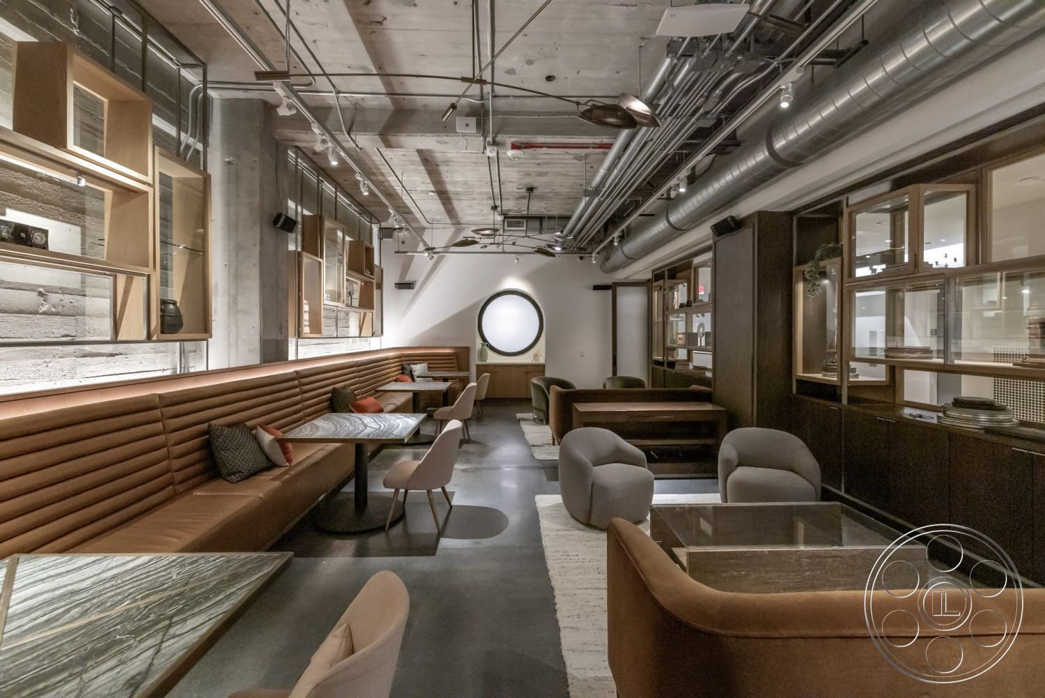 Sunset Campus - neutral color palette, natural light, interior space, polished concrete floors, exposed ductwork, concrete ceiling, round windows, leather upholstered bench seating, wood display cabinets, glass-top tables, rounded armchairs
