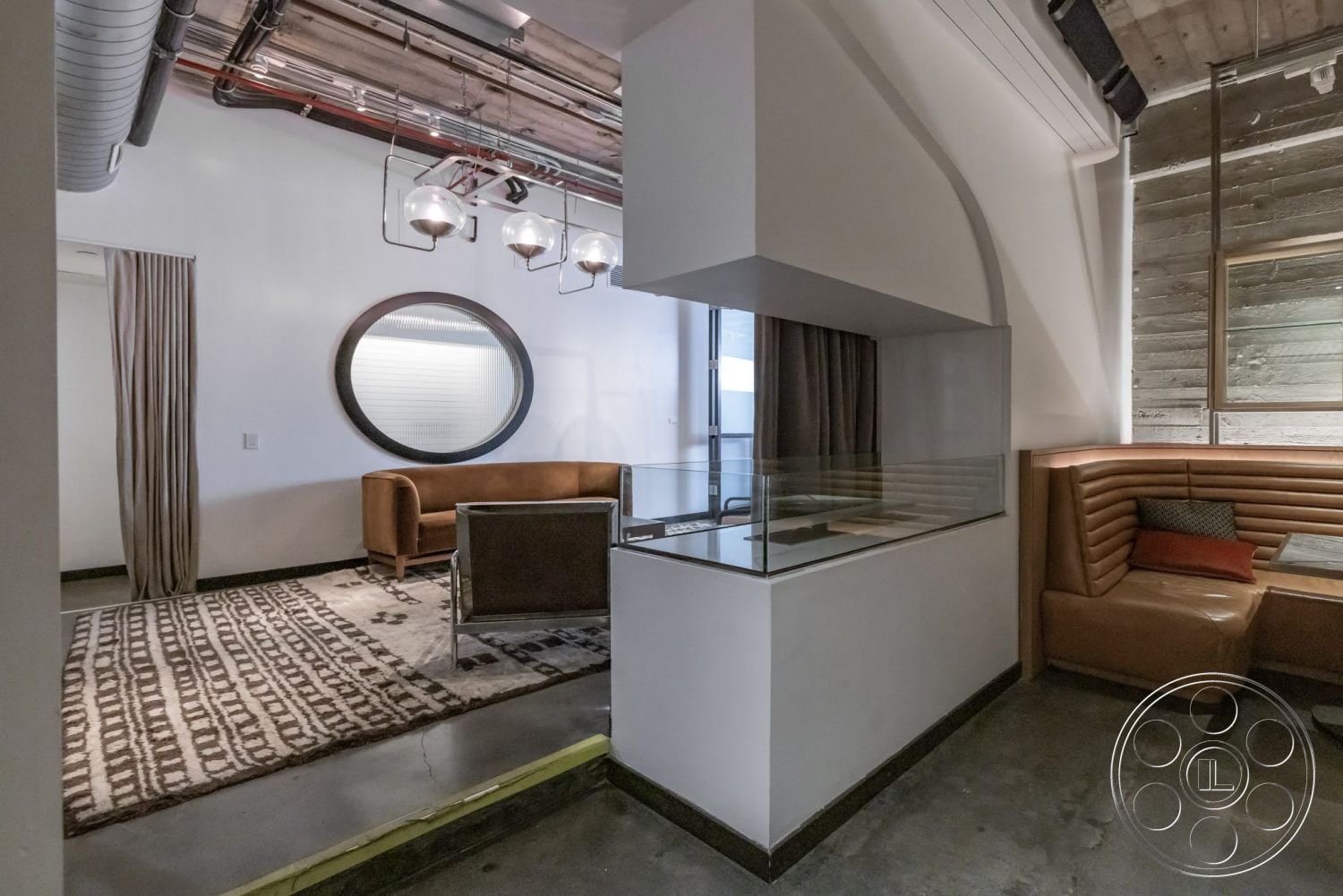 Sunset Campus - textured area rug, concrete floor, modern lighting fixtures, minimalist design elements, metal ductwork, brown leather sofa, wooden accent wall, glass partition wall, round wall mirror, fabric curtain wall, corner booth seating