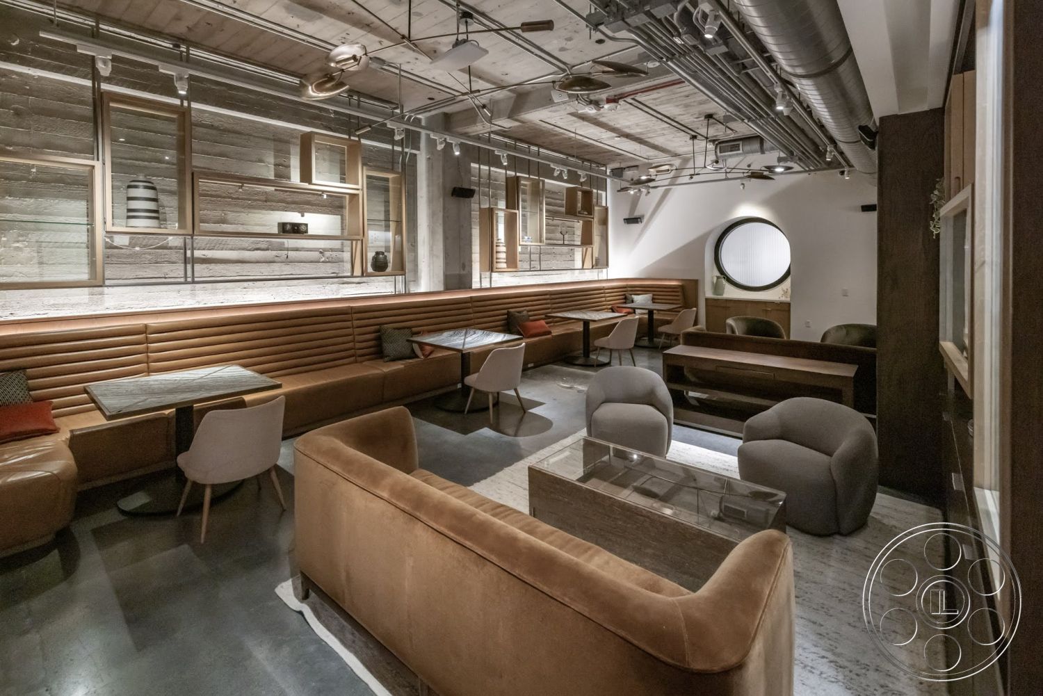 Sunset Campus - minimalist decor, polished concrete floor, wood accent wall, dark wood paneling, round window feature, grey upholstered chairs, rectangular coffee table, low-profile sectional sofa, built-in shelving units, exposed wood ceiling, modern industrial style, adjustable track lighting, leather upholstered seating