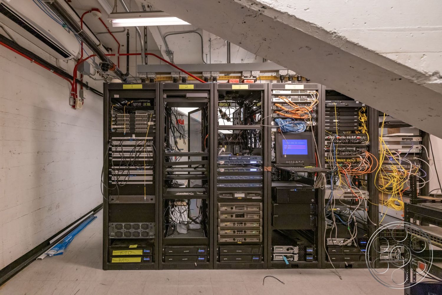 Sunset Campus - concrete flooring, concrete walls, LED ceiling lights, metal storage shelves, exposed electrical conduits, fiber optic cables, cabling infrastructure, network server racks, data center equipment, structured wiring, black server cabinets