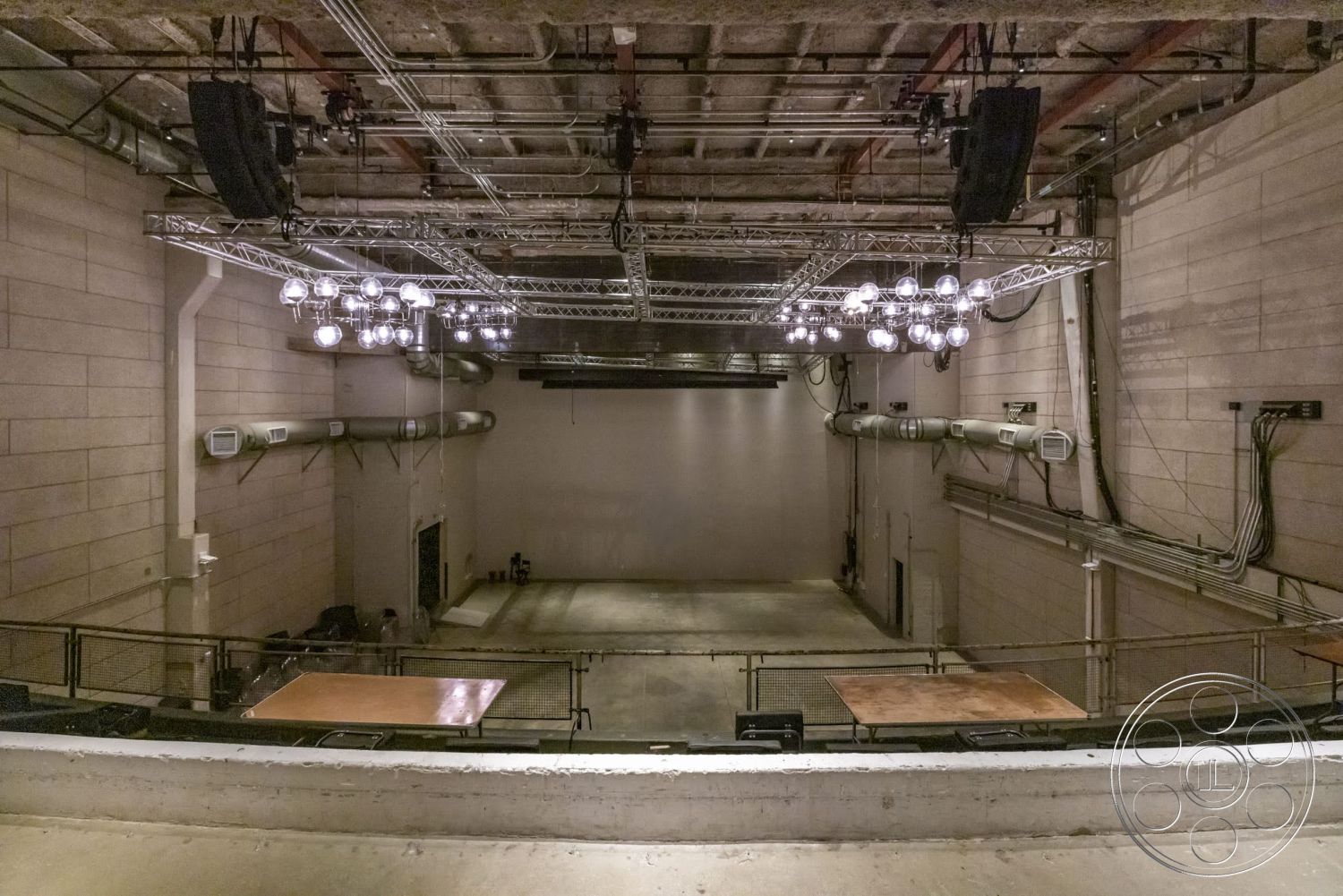 Sunset Campus - polished concrete floor, exposed concrete walls, industrial lighting fixtures, open performance space, metal grid ceiling, steel air ducts, multi-purpose venue, gallery-style interior, rear stage access