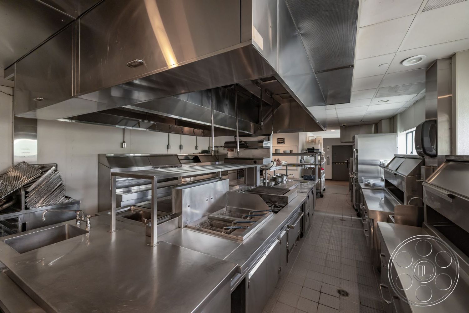Sunset Campus - tile flooring, floor-to-ceiling windows, cooking station, stainless steel kitchen appliances, open kitchen design, brightly lit interior, stainless steel countertops, kitchen prep area, commercial kitchen layout, stainless steel cabinet fronts, stainless steel ventilation hood, industrial style kitchen, exhaust ventilation system