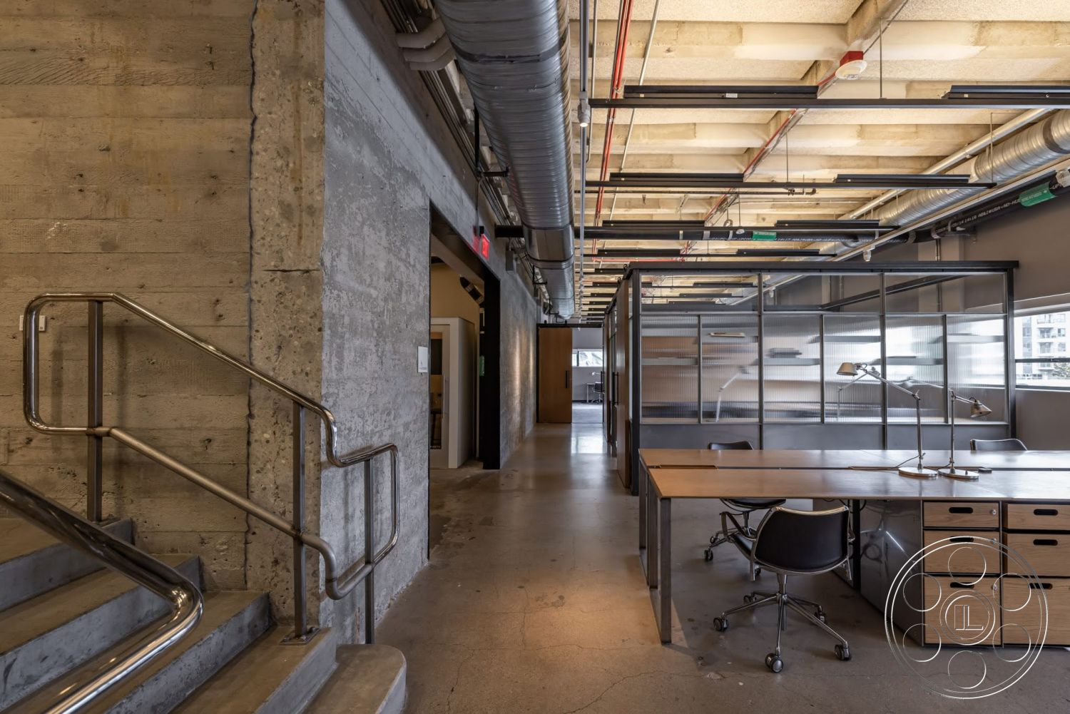 Sunset Campus - high ceilings, polished concrete flooring, exposed concrete walls, industrial lighting fixtures, open office layout, glass partition walls, contemporary office design, metal stair railing, steel ceiling beams, modern workstations, wood desk with storage