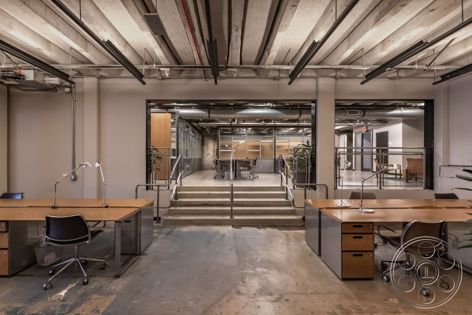 Sunset Campus - open floor plan, textured concrete walls, glass partition walls, exposed ductwork ceiling, metal office chairs, wooden office desks, steel railing staircase, exposed concrete floors, industrial style workspace, contemporary office interior