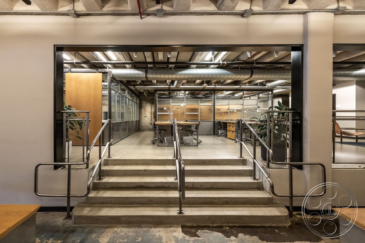 Sunset Campus - fluorescent lighting, polished concrete flooring, concrete steps, exposed ceiling beams, open office layout, glass partition walls, metal handrails, industrial style design, wooden office cabinetry, potted plants for decoration