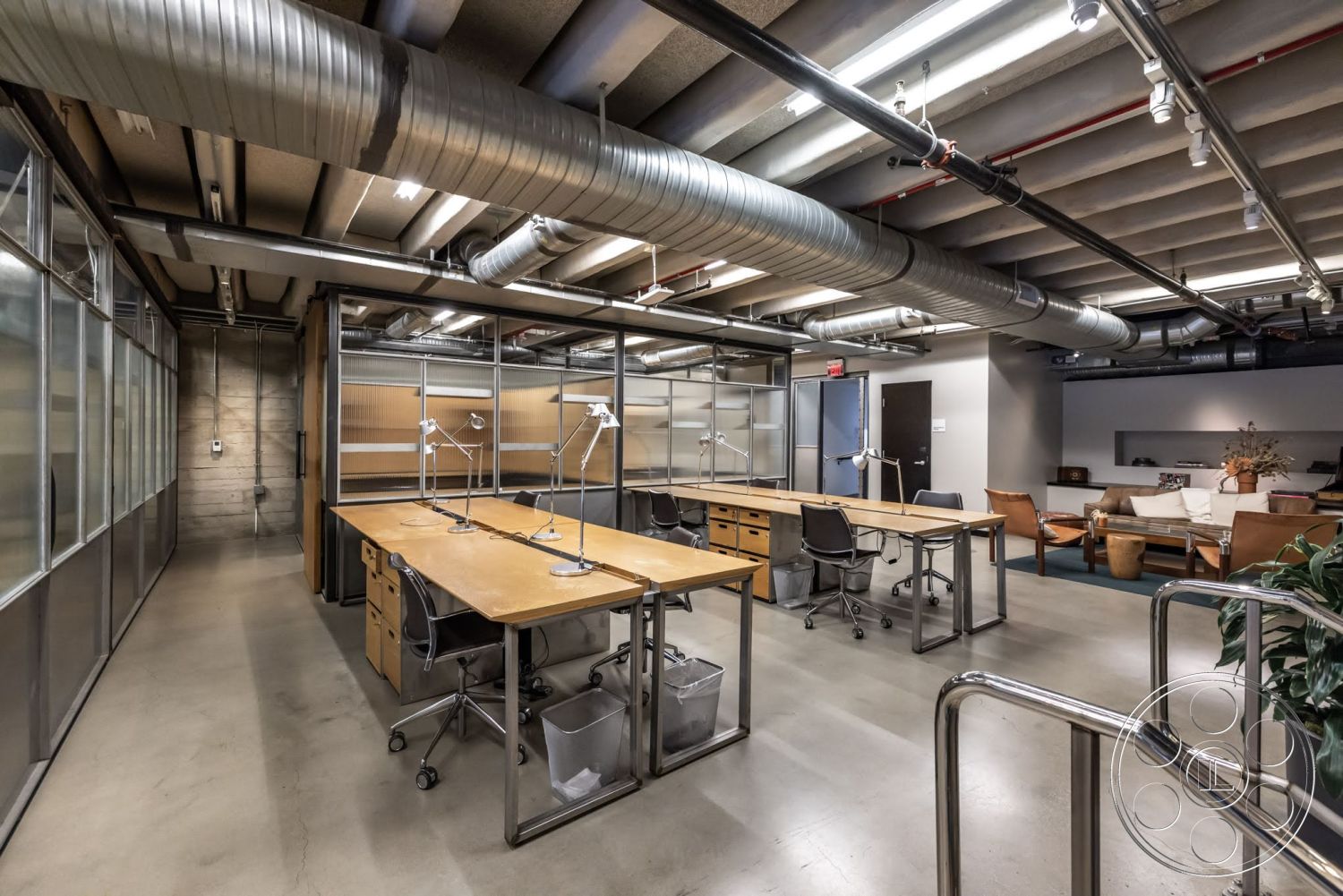Sunset Campus - neutral color palette, industrial style, open workspace, exposed concrete floor, glass partition walls, contemporary office layout, wooden desk surfaces, metal ceiling ducts, steel desk legs, modern office lighting, mixed-material furnishings