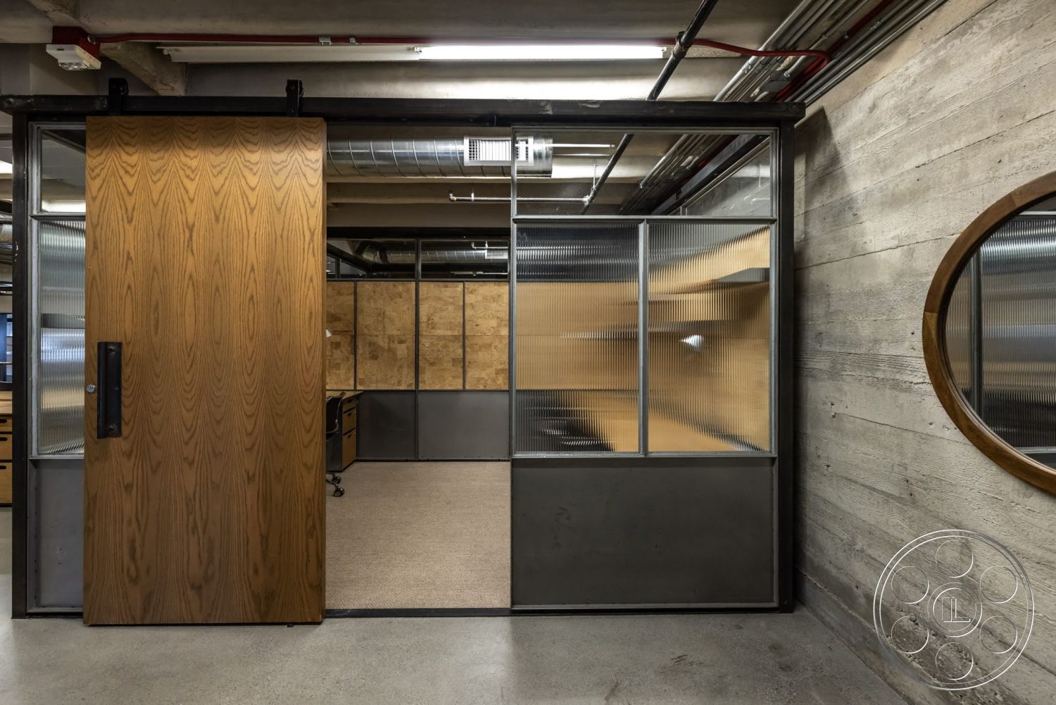 Sunset Campus - polished concrete flooring, exposed concrete walls, open office layout, glass partition walls, textured wood paneling, industrial-style lighting, circular mirror accent, wood sliding door, metal frame details