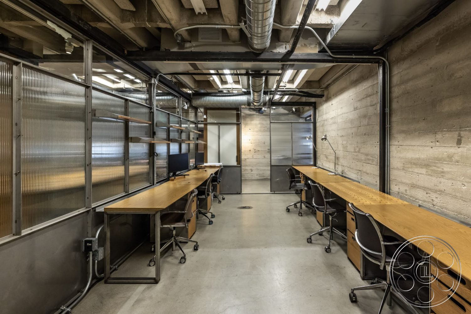 Sunset Campus - concrete flooring, exposed concrete walls, glass partition walls, modern office layout, exposed ductwork ceiling, steel structural beams, open workspace design, wooden office desks, industrial interior, metal chair bases