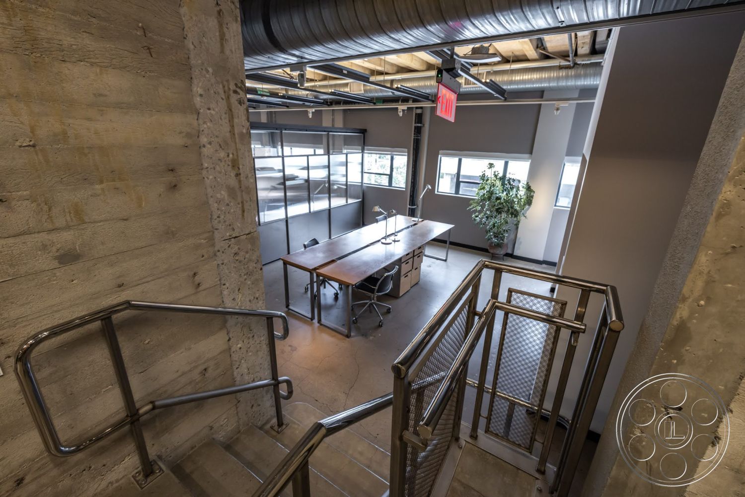 Sunset Campus - concrete flooring, large windows for natural light, glass partition walls, wooden conference table, modern office chairs, steel handrail, exposed concrete stairwell walls, open-concept office layout, industrial-style ceiling ducts, interior workspace environment