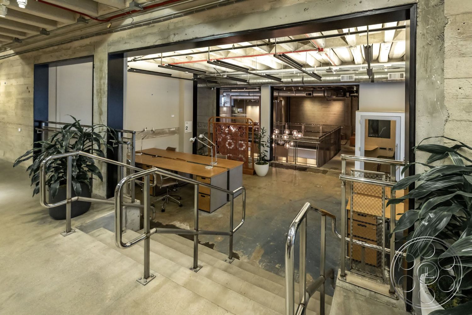 Sunset Campus - polished concrete flooring, exposed concrete walls, open office layout, glass partition walls, modern office furniture, LED strip lighting, metal ductwork ceiling, steel railing with wood accents, industrial-style staircase, planter with foliage, urban warehouse design