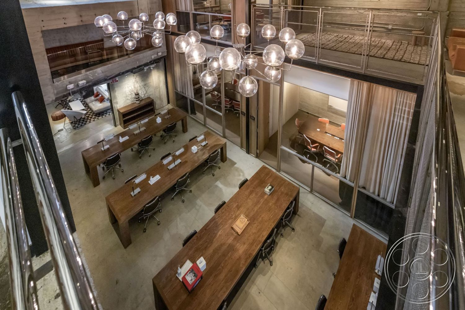 Sunset Campus - large windows, concrete floor, exposed concrete walls, metal railing, textured ceiling, glass partition walls, contemporary office design, open-plan workspace, industrial-style lighting, modern office chairs, polished concrete finish, wooden accent walls, wooden conference tables, suspended globe light fixtures, multilevel office layout