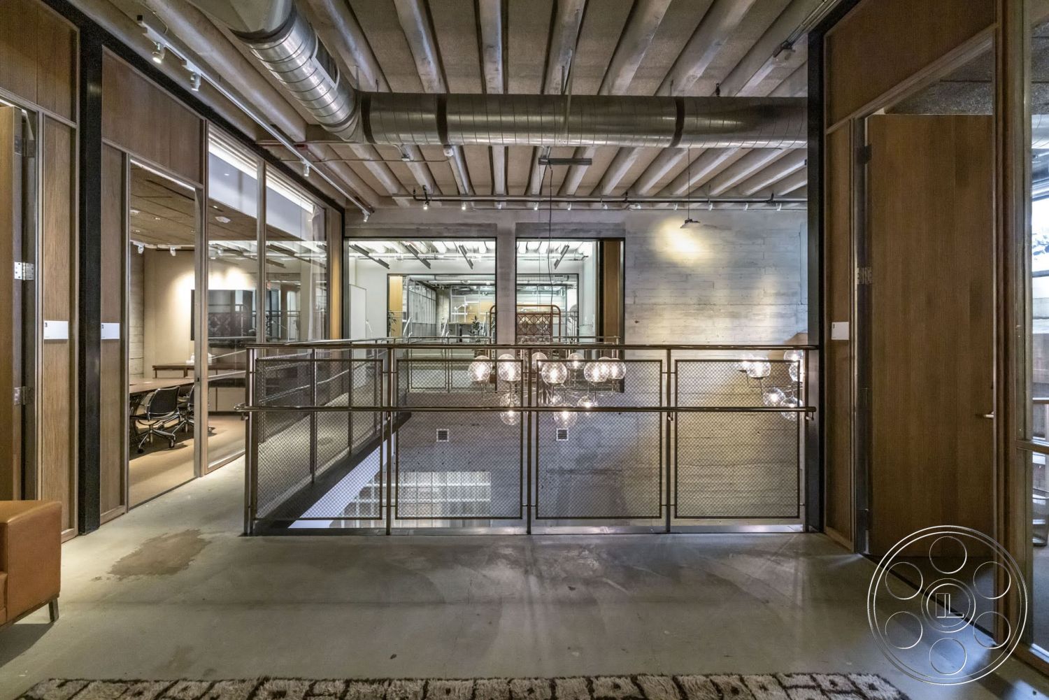 Sunset Campus - polished concrete floor, floor-to-ceiling windows, dark wood paneling, exposed concrete ceiling, open office layout, glass partition walls, wood beam ceiling, industrial style architecture, interior balcony, metal mesh railing