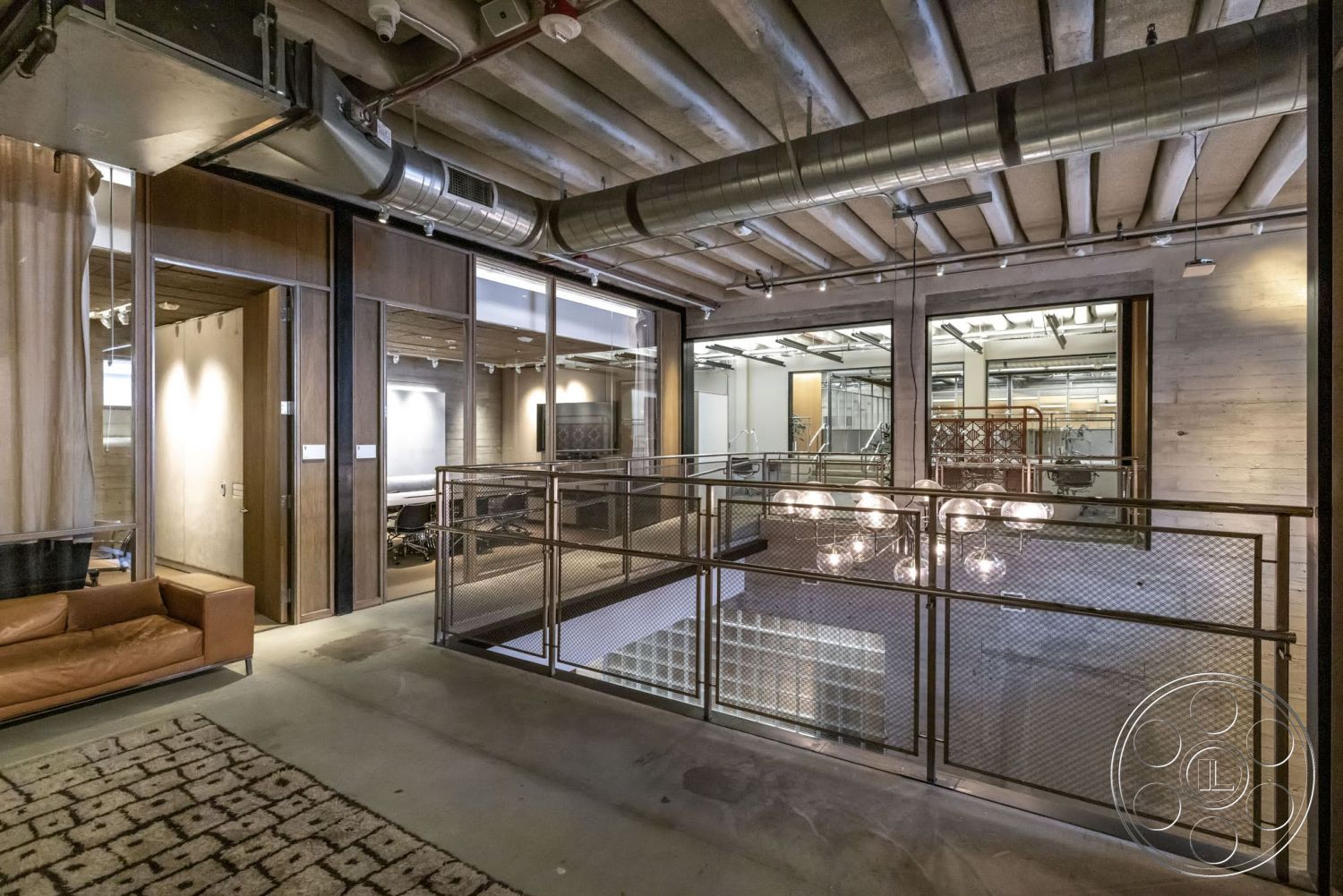 Sunset Campus - textured area rug, concrete floor, modern interior, exposed concrete walls, wooden ceiling beams, brown leather sofa, open office layout, glass partition walls, industrial-style lighting fixtures, metal mesh balcony railing