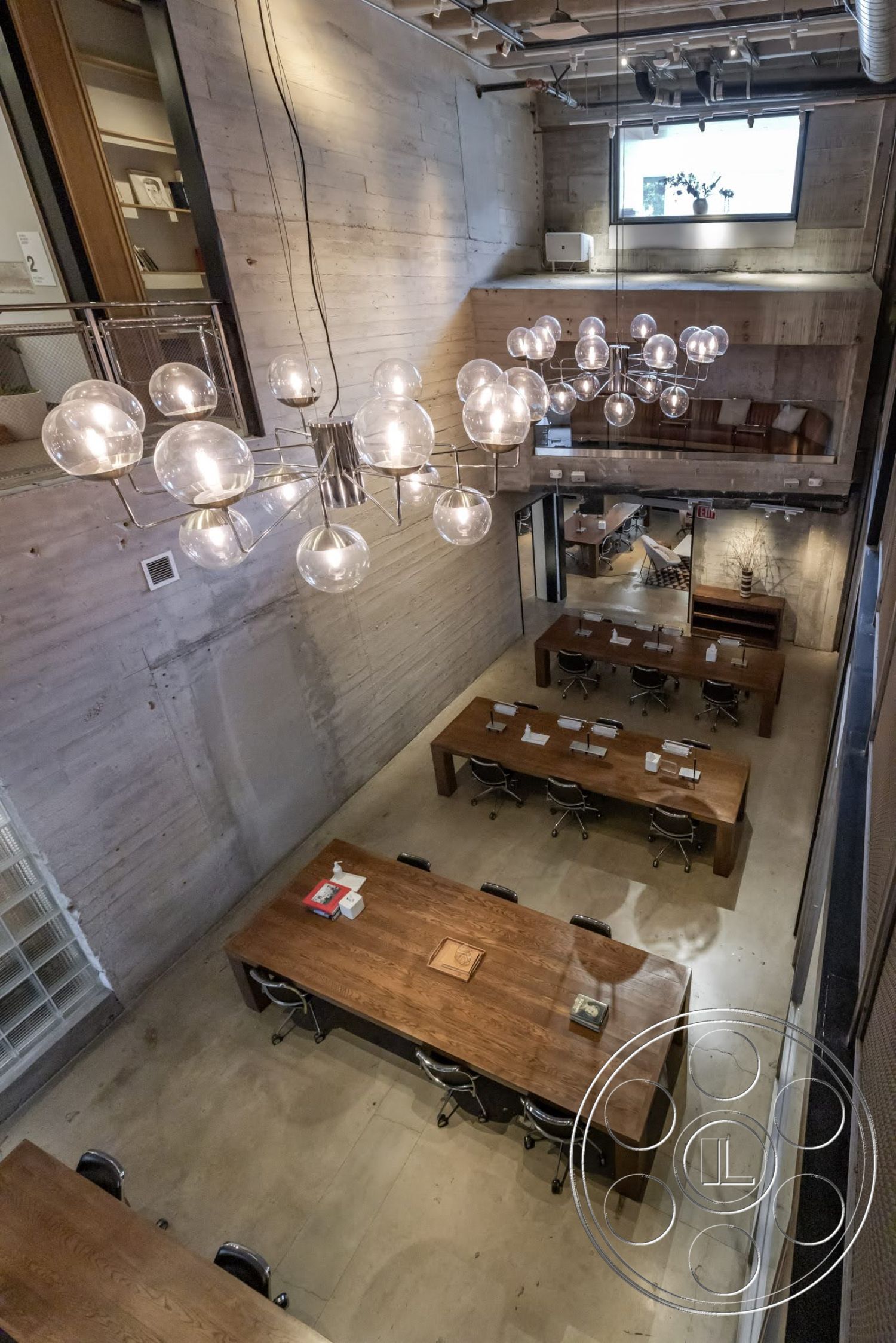 Sunset Campus - concrete flooring, exposed concrete walls, floor-to-ceiling windows, modern architectural style, glass pendant lighting, open office layout, exposed structural elements, minimalist interior design, wood conference tables, industrial ceiling details, workplace setting