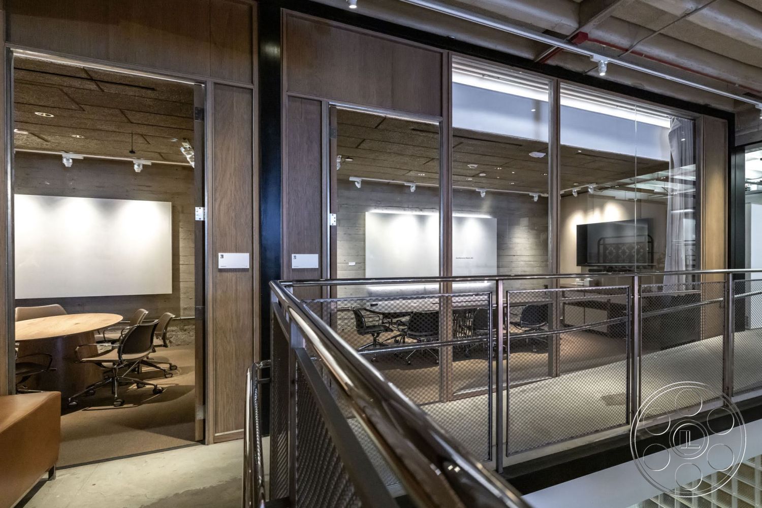 Sunset Campus - carpeted flooring, glass wall partitions, modern office design, interior office space, wood paneling on walls, exposed wood ceiling panels, leather seating area, round conference table, mesh metal railing, overhead track lighting