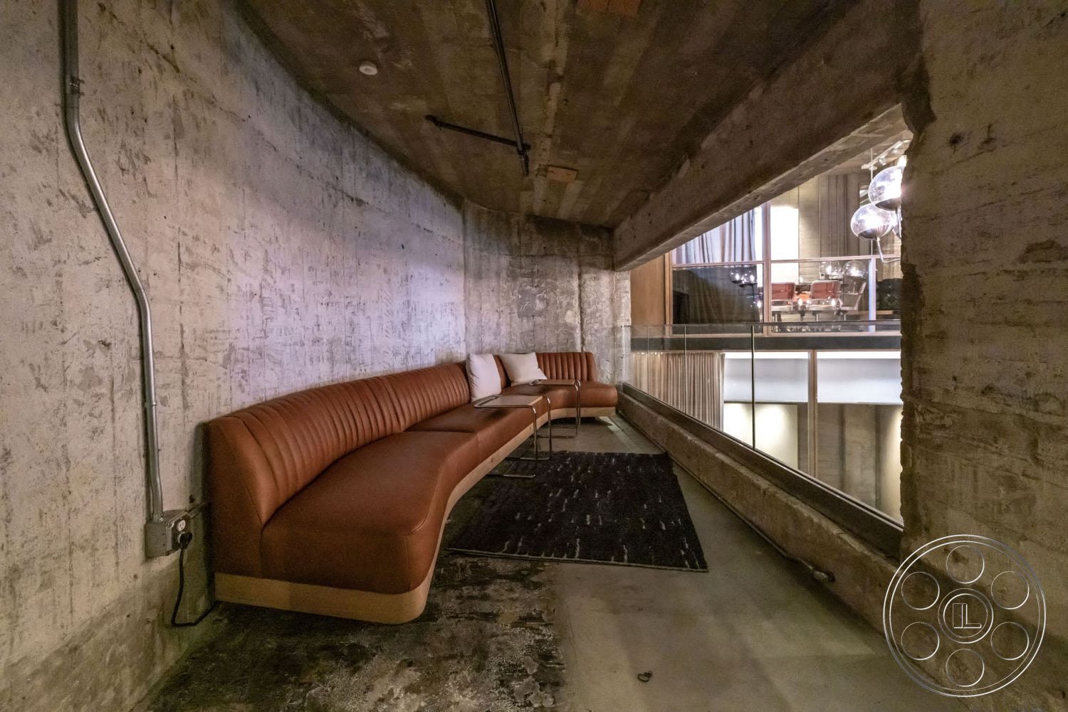 Sunset Campus - exposed concrete walls, industrial lighting fixtures, modern architectural style, curved wall design, concrete ceiling, leather sectional sofa, textured carpet flooring, floor-to-ceiling glass window, metal piping details