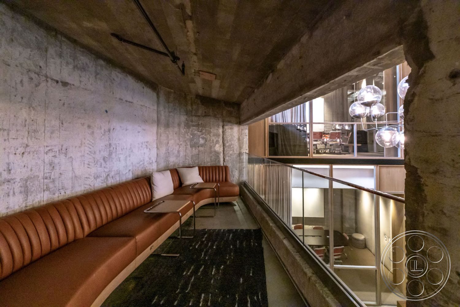 Sunset Campus - exposed concrete walls, metal railing, glass partition, concrete ceiling, textured carpet flooring, pendant light fixtures, wood panel accents, leather curved bench seating